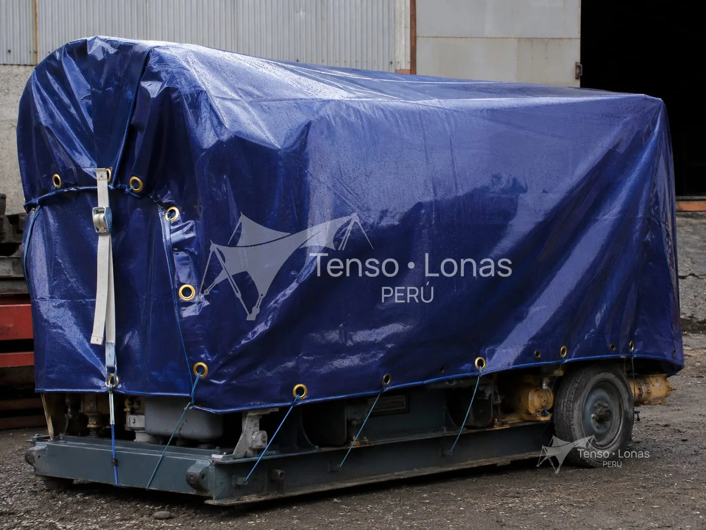 Maquinaria estacionada a la intemperie protegida con un cobertor de tarflex azul amarrado por los ojales