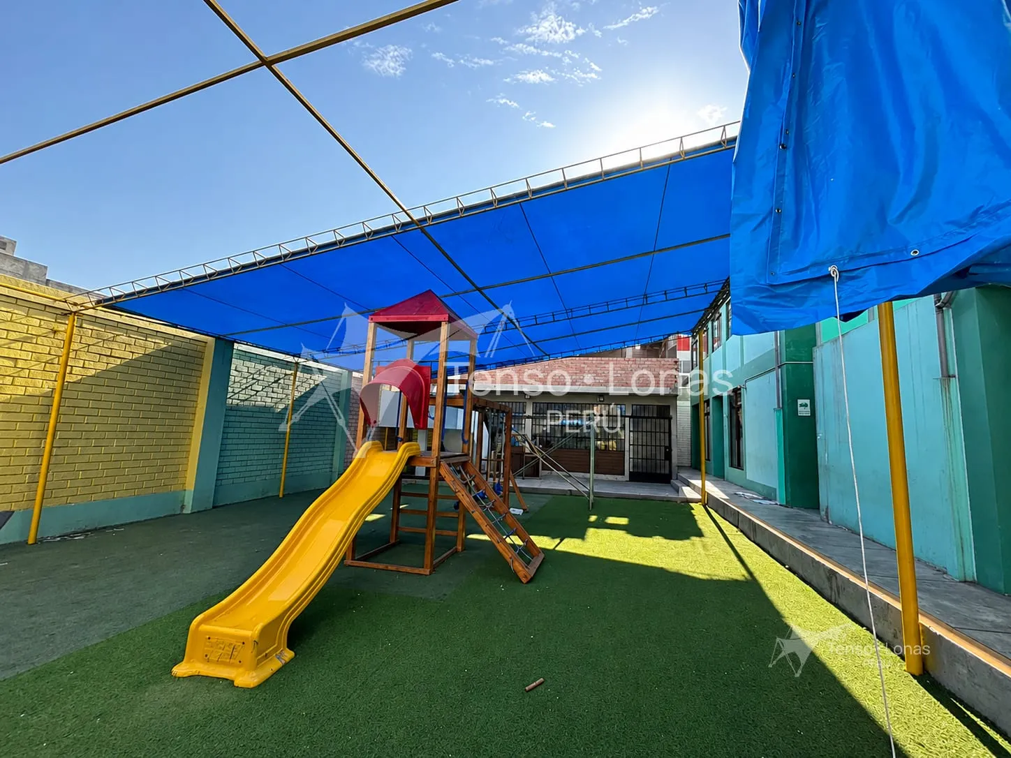 Instalación de un cobertor de lona azul sobre el patio de juegos de un colegio