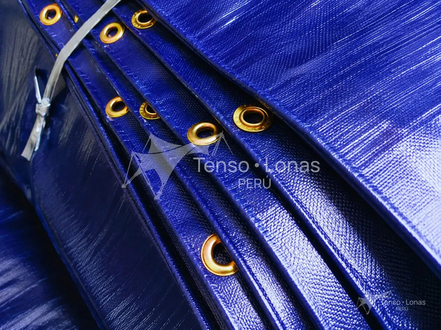 Detalle de los ojales de bronce en el borde reforzado de una manta de tarflex azul