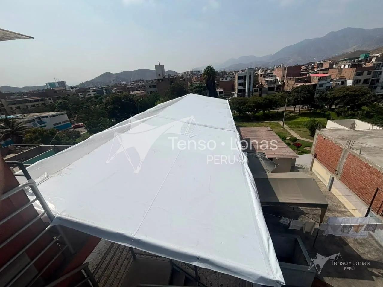 Toldo a dos aguas de lona PVC blanca instalado en la azotea, con los cerros de Lima al fondo