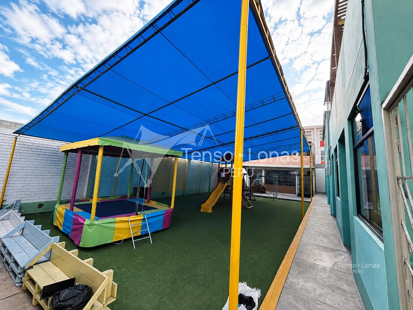 Toldo fijo de lona azul cubriendo el patio de juegos de un colegio