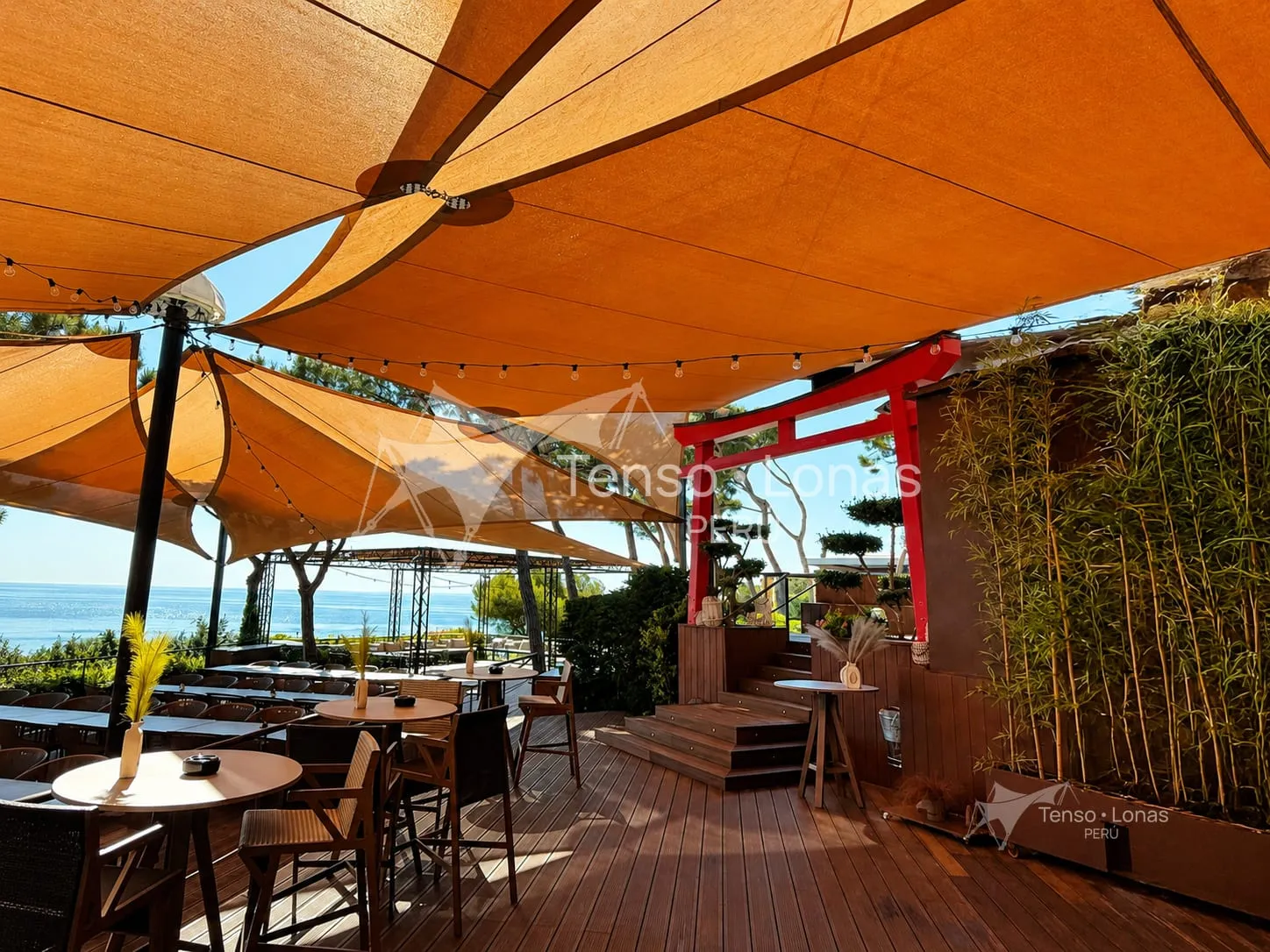 Toldos tipo vela beige sobre la terraza con mesas de un restaurante junto al mar